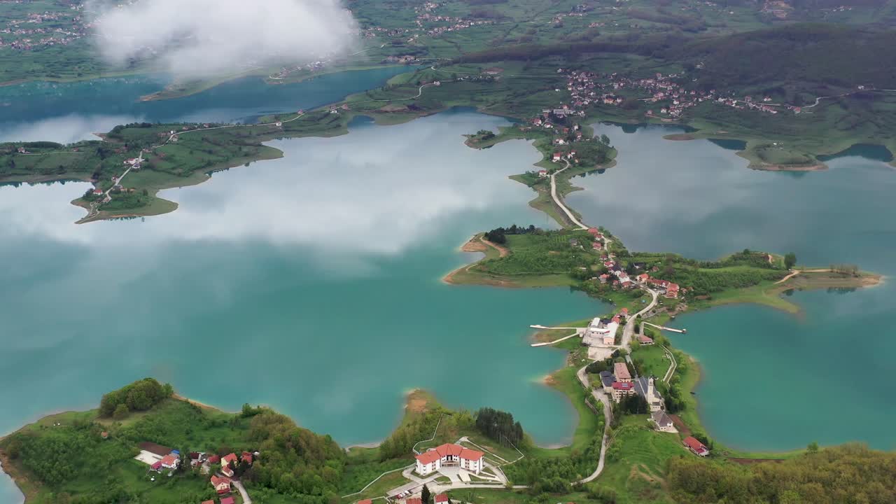 Sensational scenic view of green lake Rama water toward picturesque small island village community, Prozor-Rama, Bosnia and Herzegovina, overhead aerial approach