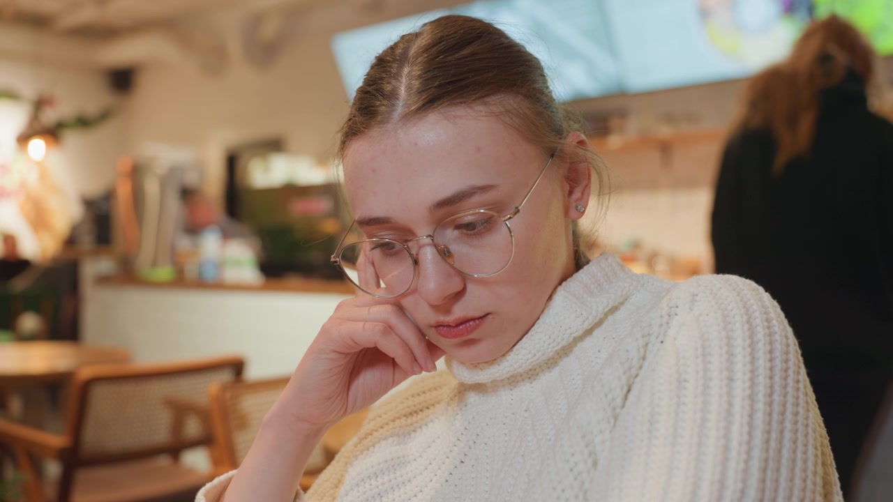 Thoughtful Young Woman in Glasses Concentrating in a Cafe