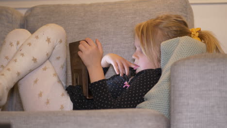 medium side view portrait of young girl watching virtual techonology tablet on living room couch at home