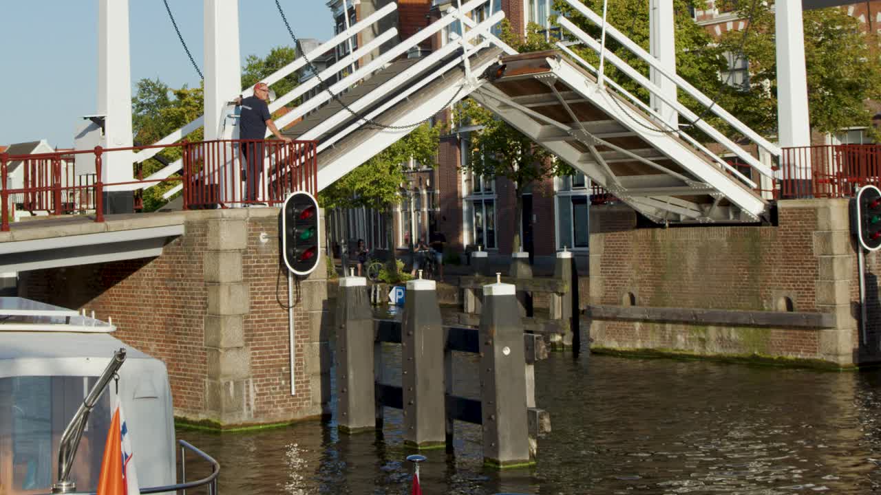 Motorboat passes under raised drawbridge in Haarlem, Netherlands, with historic canal-side buildings