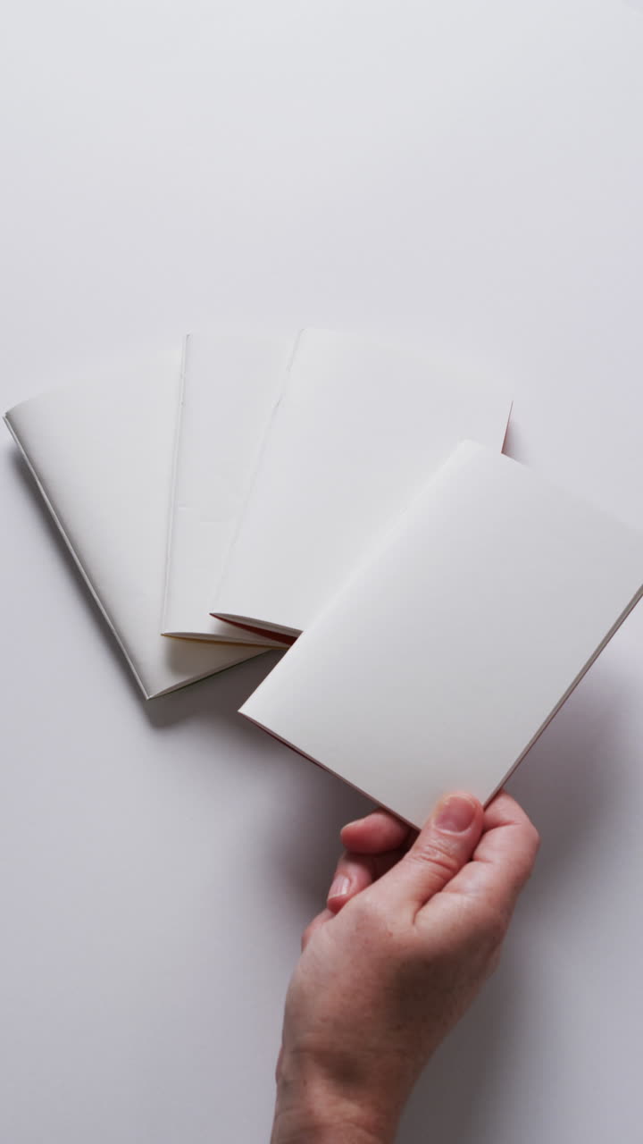 Vertical video of hand holding piece of paper over pieces of paper with copy space in slow motion