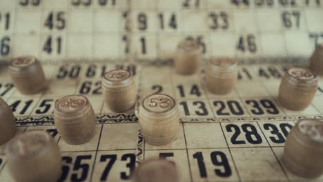 video macro de un tablero de bingo, luces de estudio, 120 fps, cámara lenta, dígitos de chips de madera, imágenes en bruto, juego de mesa de lotería, números de cartas, grúa tirando hacia atrás movimiento suave