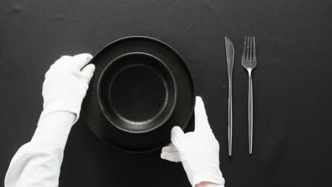 minimalist table setting with white plate, fork, and knife arranged neatly, and a gloved hand adjusting cutlery.