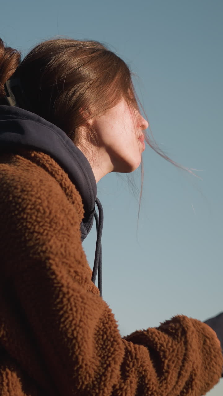 갈색 코트를 입은 소녀의 클로즈업, 그녀의 손은 그녀의 얼굴을 고, 깊이 걱정하고 생각에 빠진 것처럼 보입니다. 은 하늘 배경에 설정