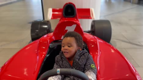 Exotisches-Zweijähriges-Afroeuropäisches-Baby,-Das-Glücklich-In-Einem-Roten-F-1-spielzeugauto-Spielt