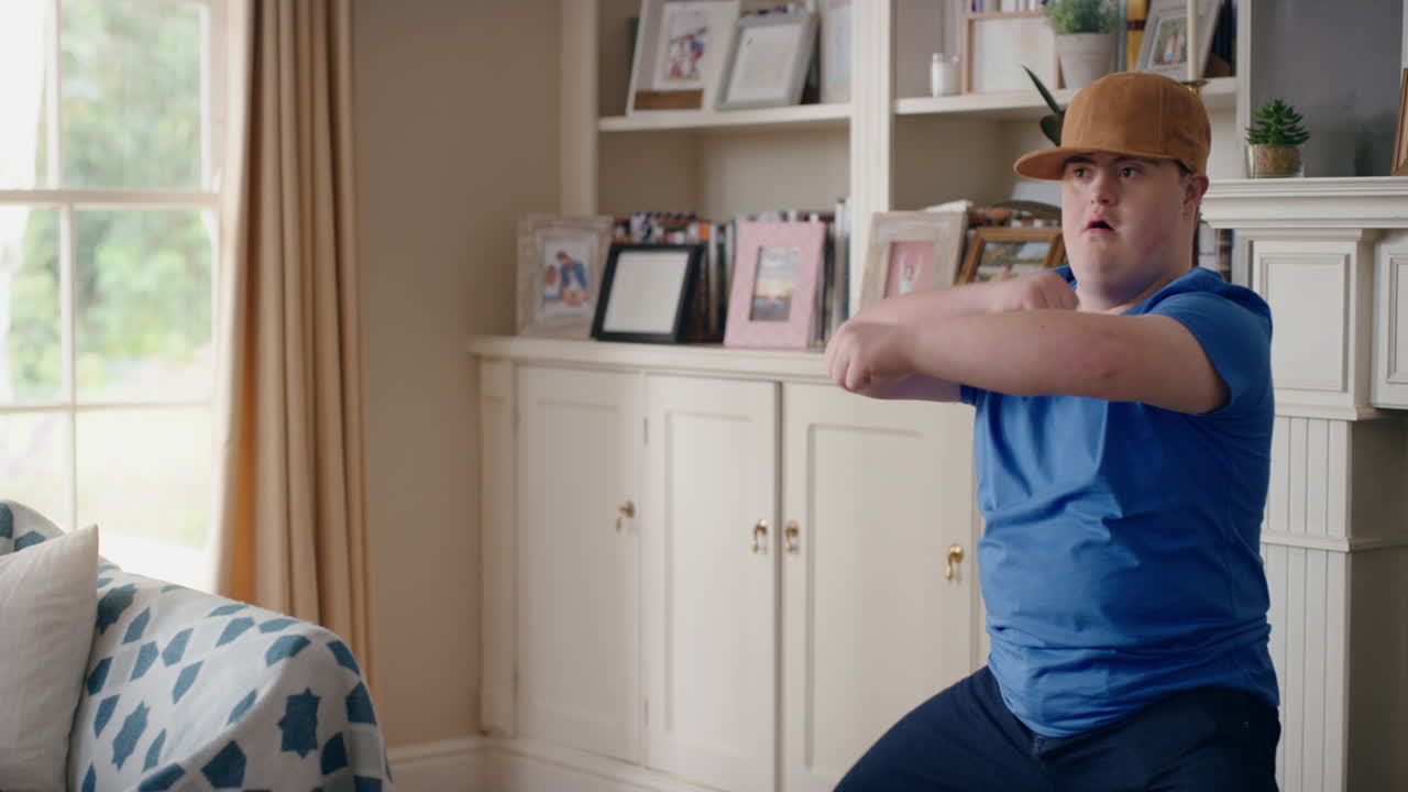 다운 증후군을 가진 재미있는 십대 소년이 거실에서 춤을 추고 특별한 요구를 가진 아이가 재미를 느끼고 어리석은 춤 움직임으로 축하하고 집에서 행복한 주말을 즐기고 4k