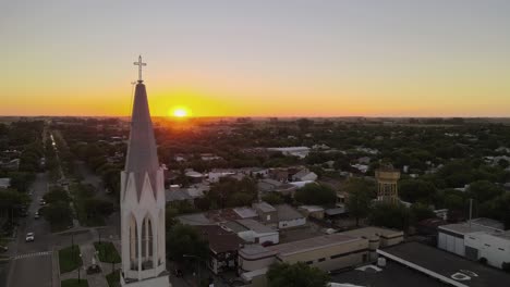 Aerial parallax shot of a church bell tower on a small town at sunset