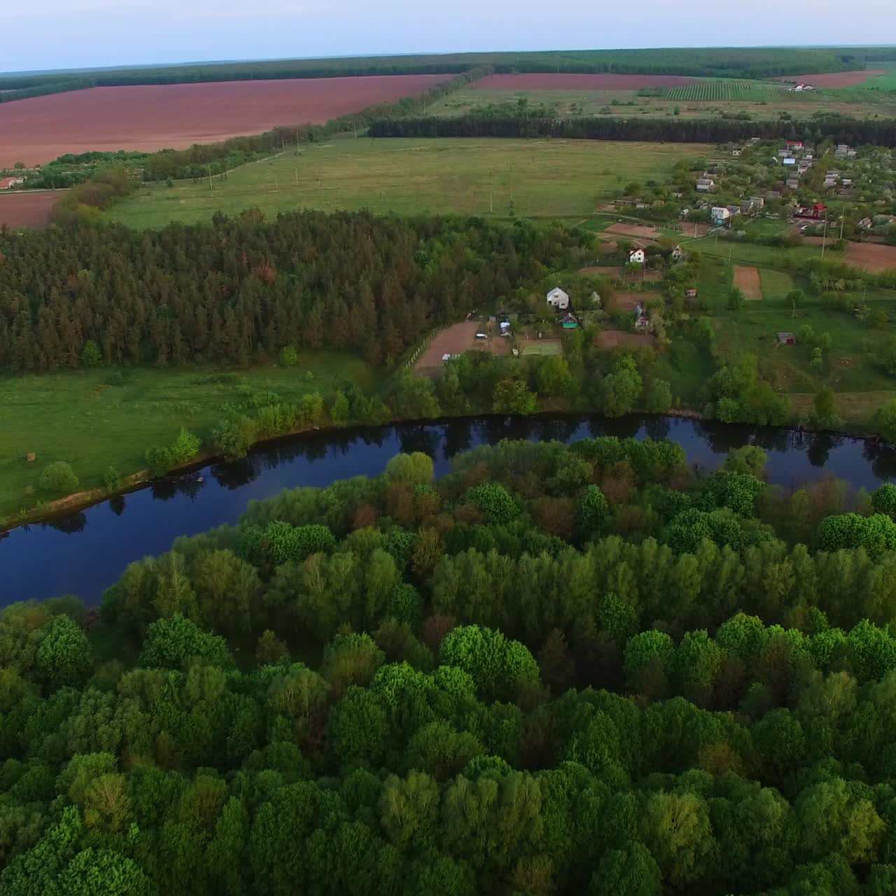 Green nature forest outlined with thin river. Rural territory nearby the woods and farmlands. Aerial view