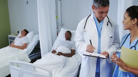 vista frontal de médicos multiétnicos discutiendo sobre el clipboard en la sala del hospital
