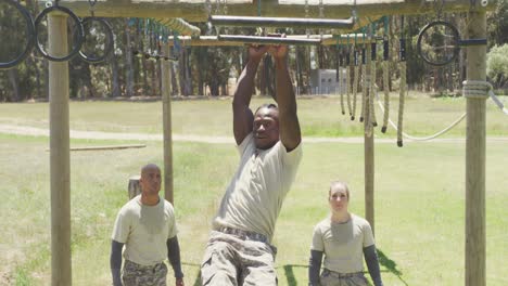 Fit-african-american-male-soldier-using-trapeze-bars-on-army-obstacle-course