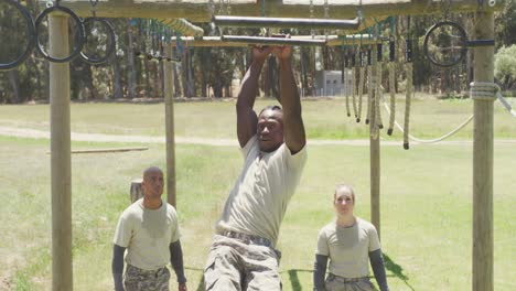 fit african american male soldier using trapeze bars on army obstacle course