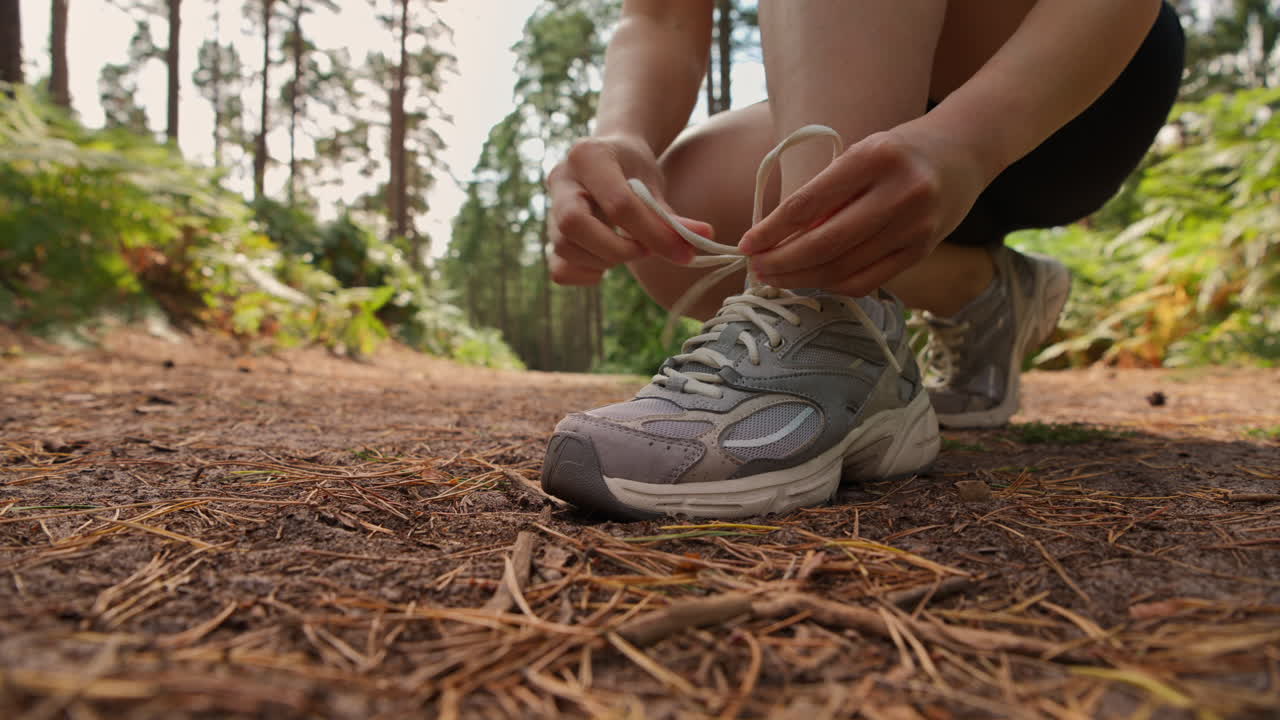 primer plano de una mujer atando los cordones de su zapato de entrenamiento antes de hacer ejercicio corriendo por la pista a través del bosque disparado en tiempo real 1