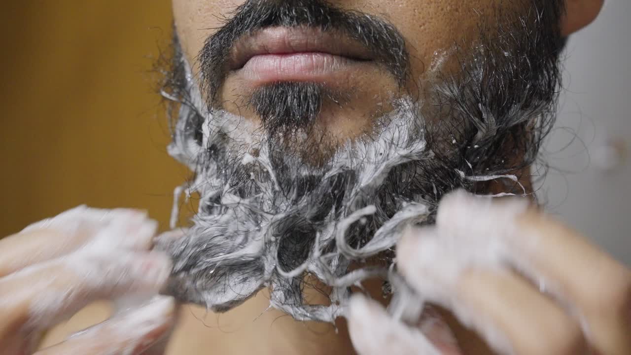 A close-up footage of a South Asian man rubbing his beard with soap and water, with a blurred background
