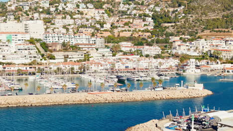 Drone-captures-yacht-dock-in-sunny-weather-with-a-beautiful-blue-sea-coast-backdrop