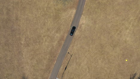 A-top-down-shot-over-a-single-car-driving-through-an-empty-park-on-a-sunny-day