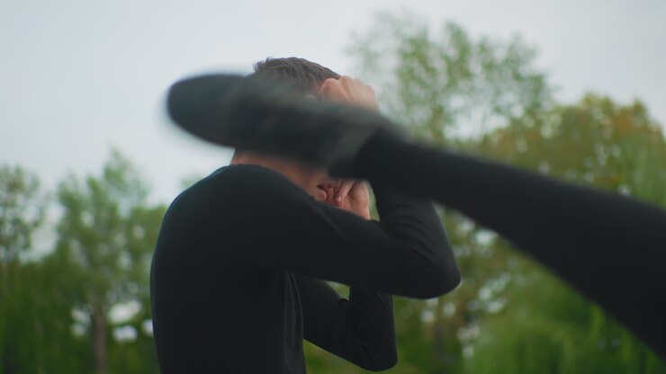 white man outdoors preparing guard, pensive warmup near trees with black long sleeve, hands at forehead and jaw, slowmotion portrait, soft overcast light, cinematic rehearsal of boxing stance