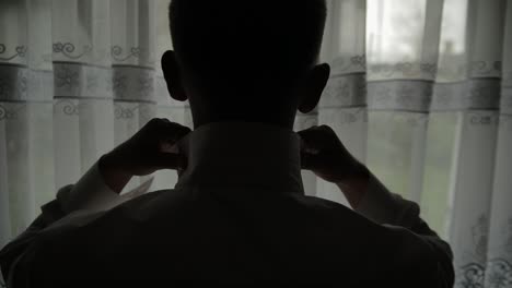 handsome groom fixes his shirt. wedding morning. silhouette. slow motion