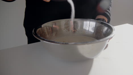 young female purring salt in a bowl with milk making dough for a cake in the kitchen at home