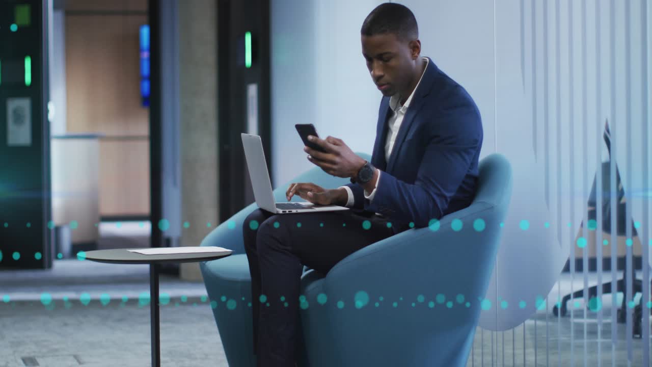 Mid-adult man working on laptop and phone in tech area passerby causing blur with turquoise overlay