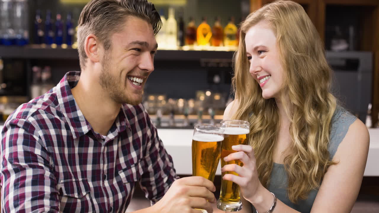 Happy caucasian couple and enjoying beers together, making a toast at bar