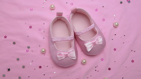 pink baby booties on pink blanket with pearls