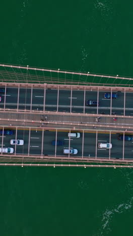 many cars moving back and forth along the huge bridge over the river. bird's eye view on the bridge at the backdrop of sea-green water. vertical video