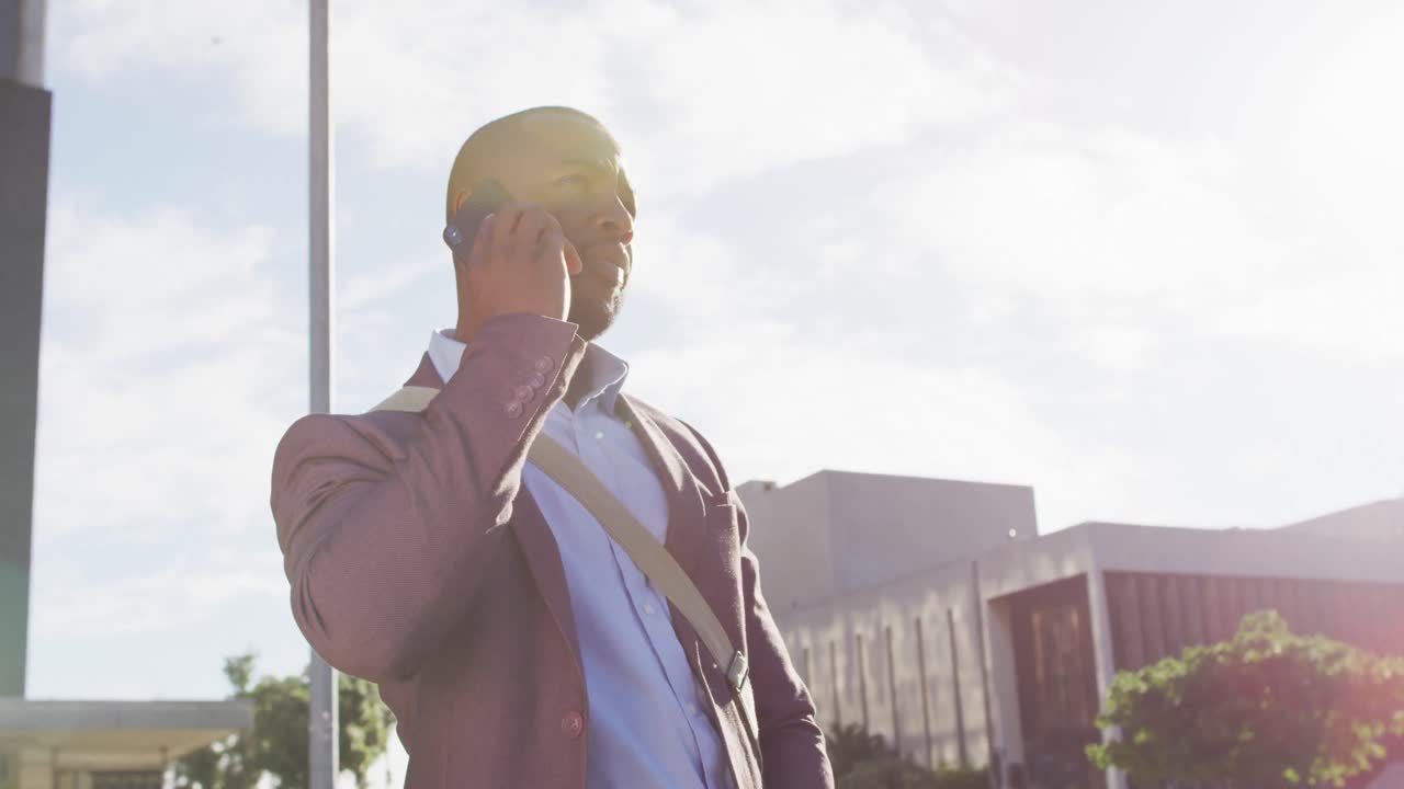 hombre afroamericano en la ciudad al sol usando un teléfono inteligente