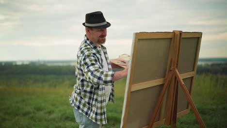 a dedicated sculptor wearing a black hat, checkered shirt, and jeans is intently painting a canvas in a serene grass field. the artist s focus and concentration on the artwork