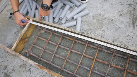 indian mason worker taking accurate measurements with a tape measure as part of a construction project, showing the wooden slab with rebar and pipes placed inside