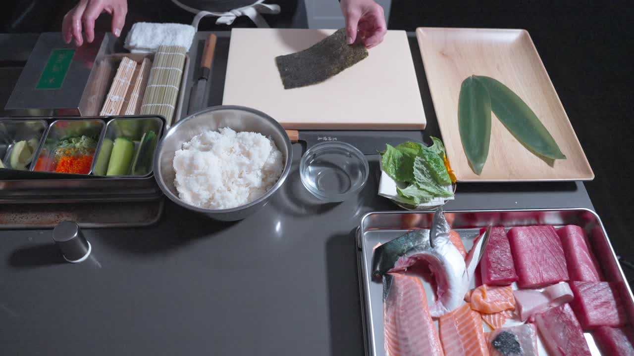 A static shot of a chef beginning the sushi-making process, carefully setting up ingredients and preparing to roll fresh sushi, showcasing the precision and technique involved in the process.