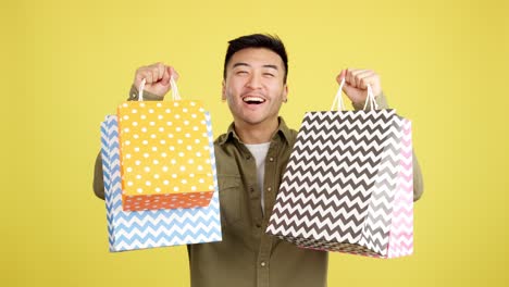 happy man showing shopping bags on yellow background