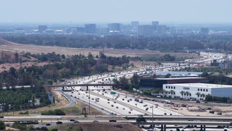 aerial drone footage over the 405 freeway in irvine, california. the shot captures busy highway traffic with the business center skyline of orange county in the background under sunny skies