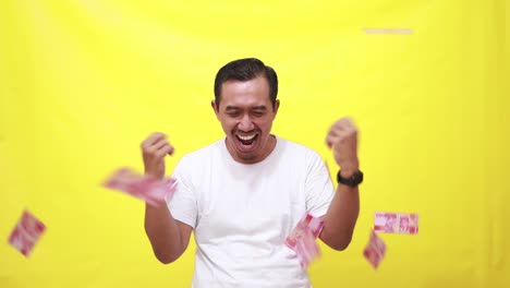 excited asian adult man celebrating success while holding indonesia banknotes and spreading it