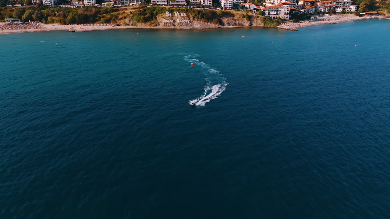 Attività nautica in acque costiere soleggiate. Una barca scivola sulle acque blu vicino a una soleggiata località balneare, esaltando il divertimento all'aria aperta