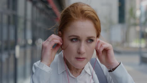 portrait beautiful young red head business woman intern puts on earphones listening to music in city enjoying relaxed urban lifestyle slow motion