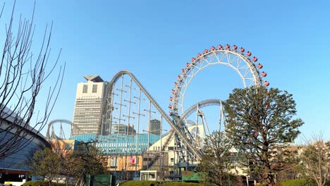 skyline view of a ferris wheel and roller coaster in an amusement park with city buildings in the background, clear day