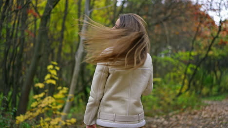 spending time in the nature in autumn. lady walks by the park with coffee, turns around and waves her hand to somebody smiling.
