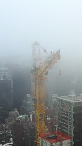 vertical drone shot circling a construction crane in middle of misty midtown, ny