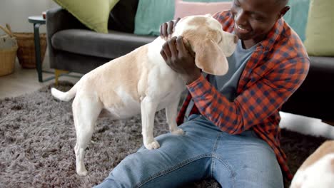 Happy-african-american-man-sitting-on-floor-at-home,-playing-with-his-pet-dogs,-slow-motion