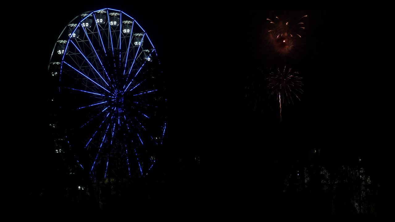 Una ruota panoramica illumina il cielo con uno spettacolo di fuochi d'artificio accanto ad essa nel cielo notturno