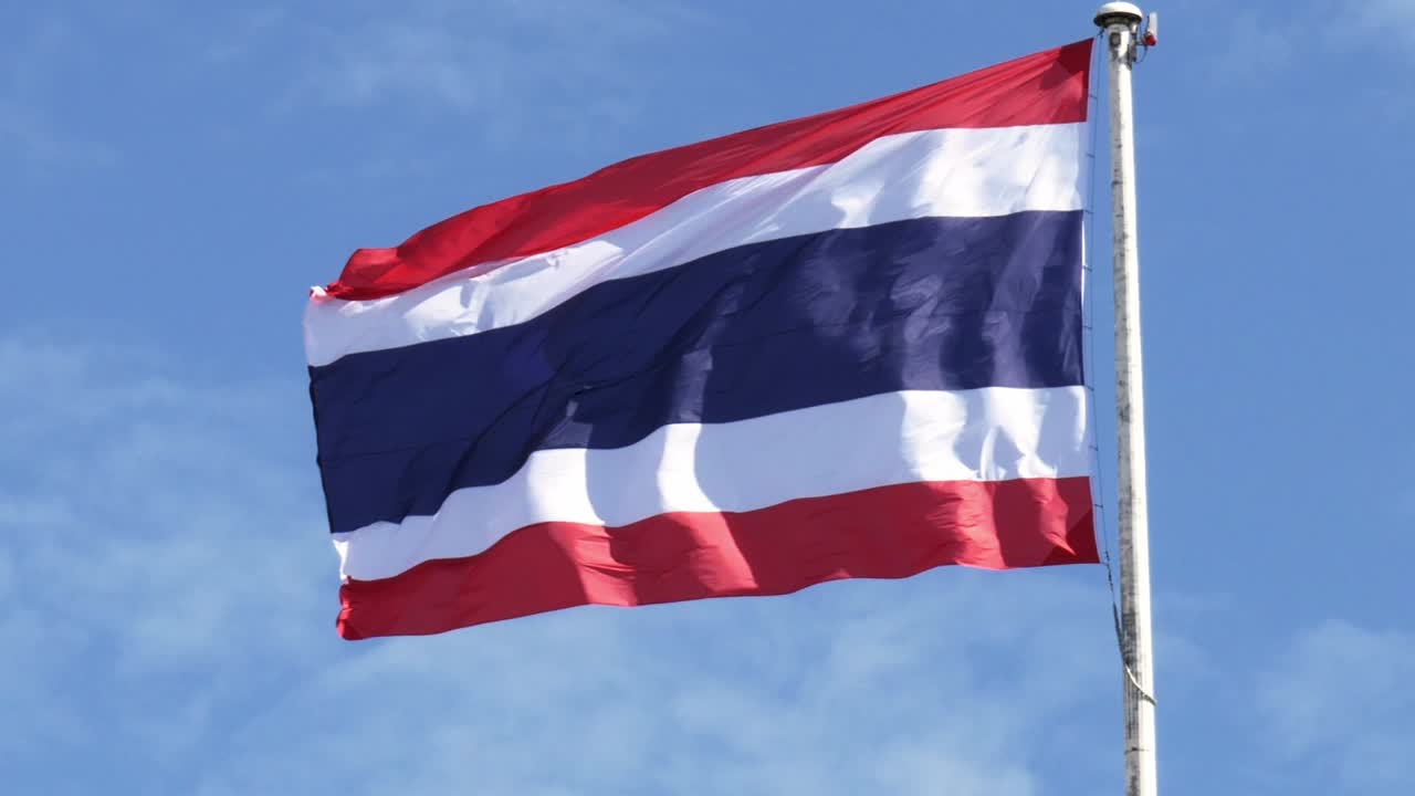 ondeando la bandera del reino de tailandia en un poste con cielo azul y nubes blancas en el fondo