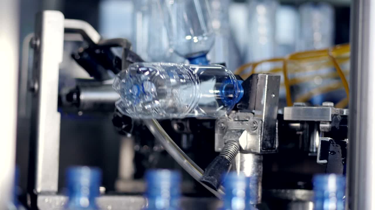 Empty water bottles grabbed from a conveyor line by a cleaning rotary wheel. 4K.