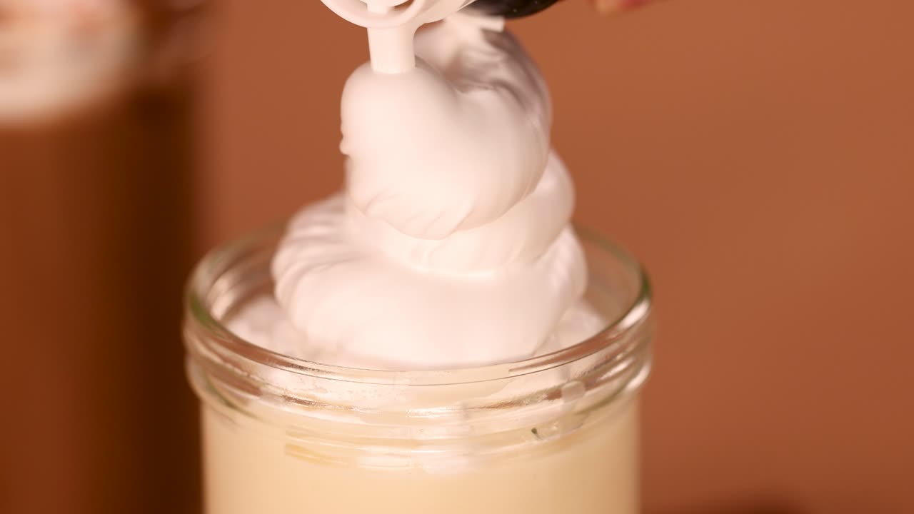 Creamy whipped topping dispensed onto vanilla milkshake in glass jar, close-up, warm lighting
