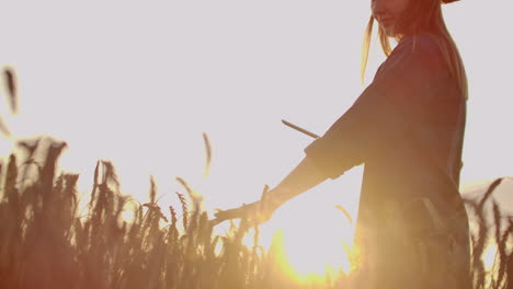 a woman farmer in a hat and a plaid shirt touches the sprouts and seeds of rye examines and enters data into the tablet computer is in the field at sunset.