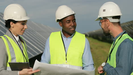 close-up view of three multiethnics farm solar engineers talking while looking at blueprint on solar plantation