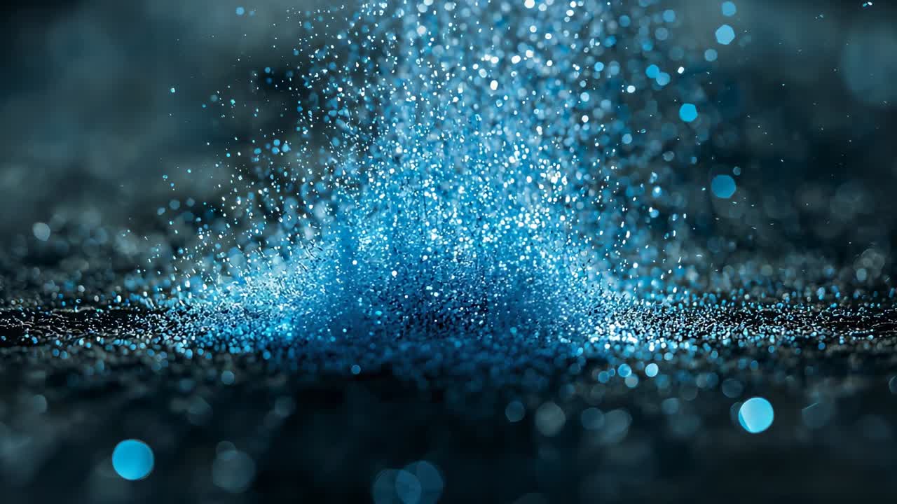 Falling blue glitter particles building conical mound on dark granular surface creating bokeh halo
