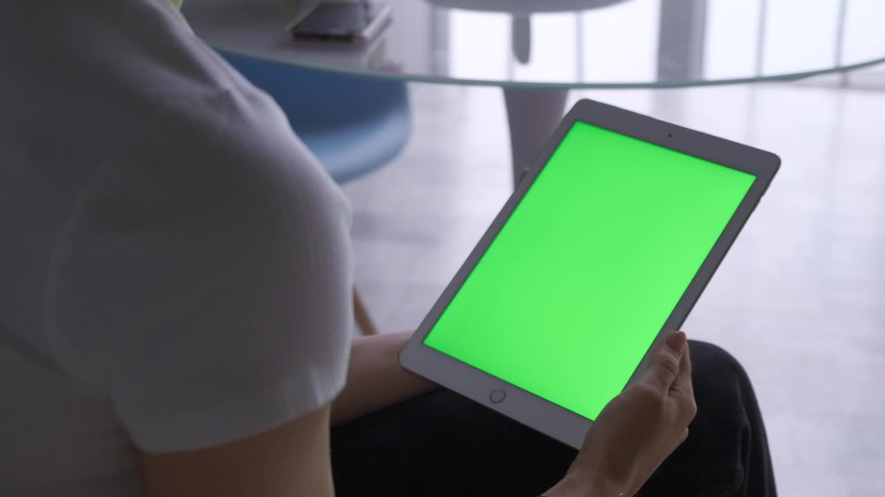 mujer sentada en el suelo y usando una tableta vertical con pantalla verde. fotografía de cerca de las manos de la mujer con el pad. sola, pantalla.