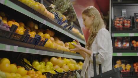 Woman-hand-choosing-lemons-at-the-grocery-store-picks-up-lemons-at-the-fruit-and-vegetable-aisle-in-a-supermarket