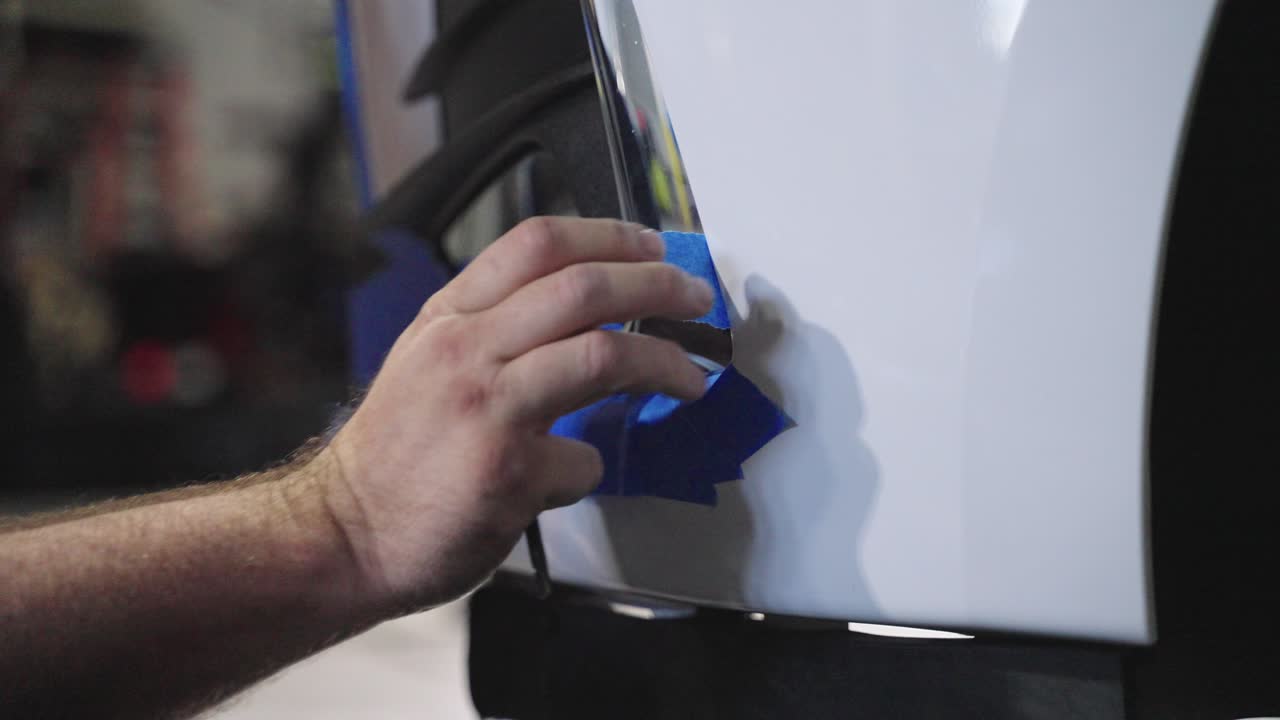 крупный план, рука анонимного механика, заклеивающего бумажной лентой передний бампер автомобиля