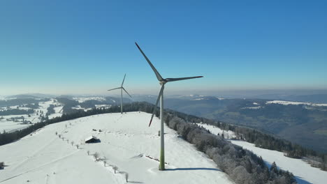 Zwei-Riesige-Moderne-Windmühlen,-Die-Sich-An-Einem-Sonnigen-Wintertag-Im-Wind-Auf-Dem-Gipfel-Des-Jura-In-Der-Schweiz-Drehen